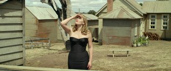 Movie still from “The Dressmaker” (2015), directed by Jocelyn Moorhouse – A woman in a black strapless dress standing in front of a tree; Medium shot, Low angle