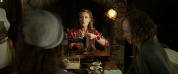 Movie still from “The Dressmaker” (2015), directed by Jocelyn Moorhouse – A woman sitting at a wooden table with a wine glass in front of her; Medium shot, Over the shoulder angle