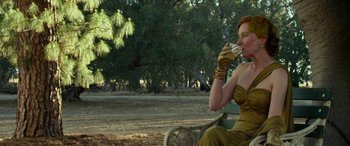 Movie still from “The Dressmaker” (2015), directed by Jocelyn Moorhouse – A woman sitting on top of a park bench drinking a glass; Medium shot, Over the shoulder angle