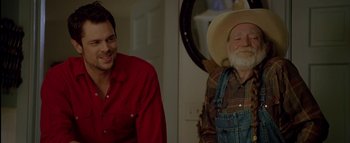 Movie still from “The Dukes of Hazzard” (2005), directed by Jay Chandrasekhar – A man in a cowboy hat is smiling next to an older man in a red shirt; Medium shot, Over the shoulder angle