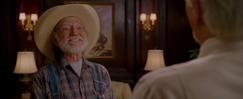 Movie still from “The Dukes of Hazzard” (2005), directed by Jay Chandrasekhar – An older man wearing a cowboy hat in front of a painting; Medium shot, Over the shoulder angle