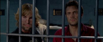 Movie still from “The Dukes of Hazzard” (2005), directed by Jay Chandrasekhar – Two men sitting next to each other behind a metal fence; Close Up shot, Over the shoulder angle