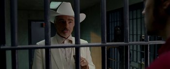 Movie still from “The Dukes of Hazzard” (2005), directed by Jay Chandrasekhar – A man in a white suit and a white cowboy hat is behind bars; Medium shot, Over the shoulder angle