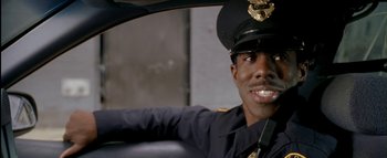 Movie still from “The Dukes of Hazzard” (2005), directed by Jay Chandrasekhar – A police officer sitting in a car smiling for the camera; Close Up shot, Over the shoulder angle
