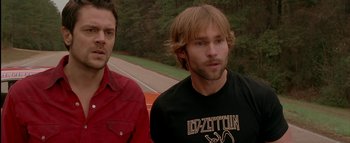 Movie still from “The Dukes of Hazzard” (2005), directed by Jay Chandrasekhar – Two men standing next to each other near a road; Medium shot, Low angle