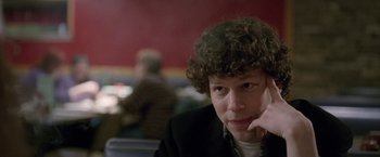 Movie still from “The End of the Tour” (2015), directed by James Ponsoldt – A man with curly hair sitting at a table with his hand under his chin; Close Up shot, Over the shoulder angle