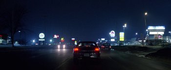 Movie still from “The End of the Tour” (2015), directed by James Ponsoldt – Cars driving down a street at night in the dark; Extreme Wide shot, High angle