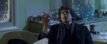 Movie still from “The End of the Tour” (2015), directed by James Ponsoldt – A man sitting at a table holding a pair of scissors; Medium shot, Over the shoulder angle