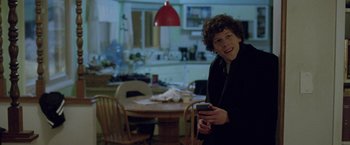 Movie still from “The End of the Tour” (2015), directed by James Ponsoldt – A young man holding a cell phone in his hand; Medium shot, Over the shoulder angle