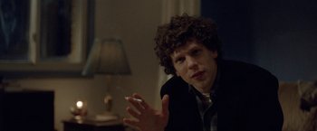 Movie still from “The End of the Tour” (2015), directed by James Ponsoldt – A man with curly hair is sitting in front of a lamp; Close Up shot, Over the shoulder angle