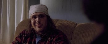 Movie still from “The End of the Tour” (2015), directed by James Ponsoldt – A man sitting on a couch wearing glasses and a hat; Close Up shot, Over the shoulder angle