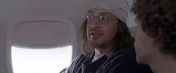 Movie still from “The End of the Tour” (2015), directed by James Ponsoldt – A man with long hair and glasses sitting on a plane; Close Up shot, Over the shoulder angle