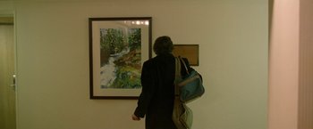 Movie still from “The End of the Tour” (2015), directed by James Ponsoldt – A woman standing in front of a painting of a stream; Medium shot, High angle