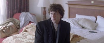 Movie still from “The End of the Tour” (2015), directed by James Ponsoldt – A young man sitting on top of a bed in front of a lamp; Medium shot, Over the shoulder angle