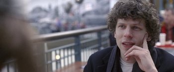Movie still from “The End of the Tour” (2015), directed by James Ponsoldt – A young man with curly brown hair wearing a black jacket; Close Up shot, Over the shoulder angle