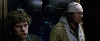 Movie still from “The End of the Tour” (2015), directed by James Ponsoldt – Two people standing next to each other on a train; Medium shot, Over the shoulder angle