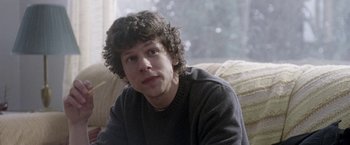 Movie still from “The End of the Tour” (2015), directed by James Ponsoldt – A young man sitting on top of a couch in front of a window; Close Up shot, Over the shoulder angle