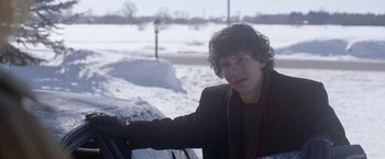 Movie still from “The End of the Tour” (2015), directed by James Ponsoldt – A man leaning on the side of a car in the snow; Medium shot, Over the shoulder angle