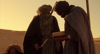 Movie still from “The English Patient” (1996), directed by Anthony Minghella – Two men are standing in the desert looking at a piece of wood; Medium shot, Low angle