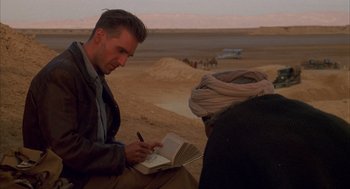Movie still from “The English Patient” (1996), directed by Anthony Minghella – A man writing in a notebook while sitting on the ground; Medium shot, Over the shoulder angle