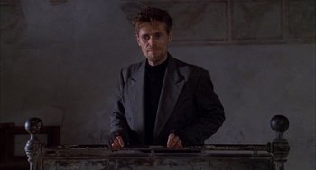 Movie still from “The English Patient” (1996), directed by Anthony Minghella – A man wearing a suit and tie standing in front of a wall; Medium shot, Low angle