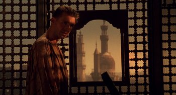 Movie still from “The English Patient” (1996), directed by Anthony Minghella – A man standing in front of a window with a view of a building; Medium shot, Low angle
