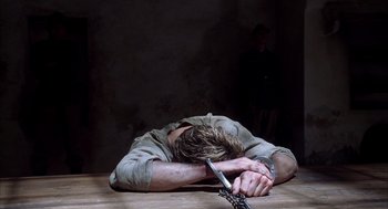 Movie still from “The English Patient” (1996), directed by Anthony Minghella – A man with his head on a table with a knife in his hand; Medium shot, High angle