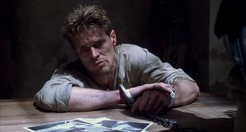 Movie still from “The English Patient” (1996), directed by Anthony Minghella – A man sitting at a wooden table holding a cell phone; Close Up shot, High angle