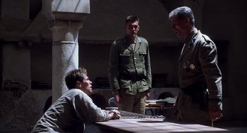 Movie still from “The English Patient” (1996), directed by Anthony Minghella – A group of men standing next to each other in a room; Medium shot, Over the shoulder angle