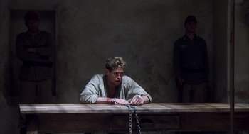 Movie still from “The English Patient” (1996), directed by Anthony Minghella – A man sitting at a table with chains around his neck; Wide shot, High angle