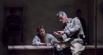 Movie still from “The English Patient” (1996), directed by Anthony Minghella – Two men are sitting on a bench and one of the men is holding a chain; Medium shot, Over the shoulder angle