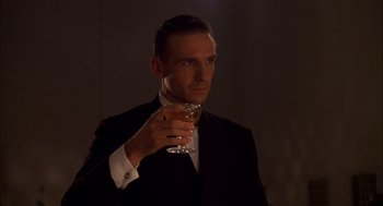 Movie still from “The English Patient” (1996), directed by Anthony Minghella – A man in a suit holding a glass of wine; Close Up shot, Low angle