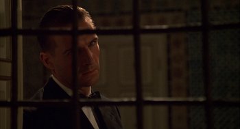 Movie still from “The English Patient” (1996), directed by Anthony Minghella – A man in a suit and bow tie looking out of a jail cell; Close Up shot, Low angle