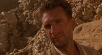 Movie still from “The English Patient” (1996), directed by Anthony Minghella – A person wearing a jacket near rocks; Close Up shot, Over the shoulder angle