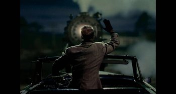 Movie still from “The Fabelmans” (2022), directed by Steven Spielberg – A man in a suit waves at a train engine; Medium shot, Over the shoulder angle