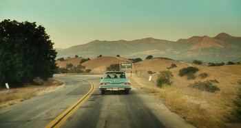 Movie still from “The Fabelmans” (2022), directed by Steven Spielberg – A car driving down a road with mountains in the background; Extreme Wide shot, High angle