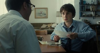 Movie still from “The Fabelmans” (2022), directed by Steven Spielberg – A man sitting at a table holding a piece of paper in front of another man; Medium shot, Over the shoulder angle