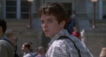 Movie still from “The Faculty” (1998), directed by Robert Rodriguez – A young man with a backpack standing in front of a crowd; Close Up shot, Low angle