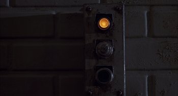 Movie still from “The Faculty” (1998), directed by Robert Rodriguez – An orange traffic light on the side of a building; Extreme Close Up shot, Overhead angle