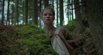 Movie still from “The Field Guide to Evil” (2018), directed by Can Evrenol – A young woman holding a bag while standing next to a tree; Medium shot, Low angle