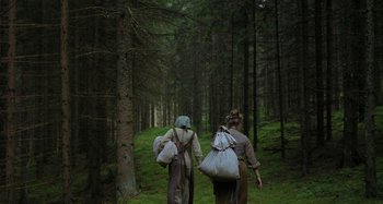 Movie still from “The Field Guide to Evil” (2018), directed by Can Evrenol – Two people walking through the woods carrying bags; Wide shot, Low angle