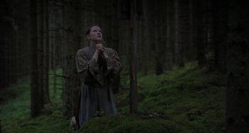 Movie still from “The Field Guide to Evil” (2018), directed by Can Evrenol – A man standing in the middle of a forest with his hands clasped; Medium shot, Low angle