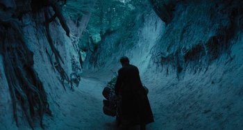 Movie still from “The Field Guide to Evil” (2018), directed by Can Evrenol – A man walking down a snow covered path with bags; Wide shot, High angle