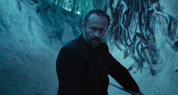 Movie still from “The Field Guide to Evil” (2018), directed by Can Evrenol – A man in a black jacket standing next to snow covered trees; Medium shot, High angle
