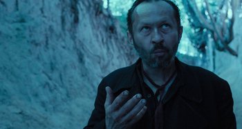 Movie still from “The Field Guide to Evil” (2018), directed by Can Evrenol – A man with a beard and a red neck tie; Close Up shot, Low angle