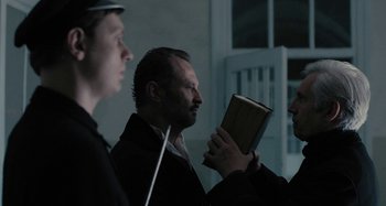 Movie still from “The Field Guide to Evil” (2018), directed by Can Evrenol – A group of men standing next to each other holding a book; Medium shot, Over the shoulder angle