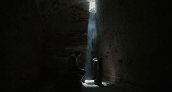 Movie still from “The Field Guide to Evil” (2018), directed by Can Evrenol – A person sitting in a dark room with a light shining through the window; Extreme Wide shot, High angle