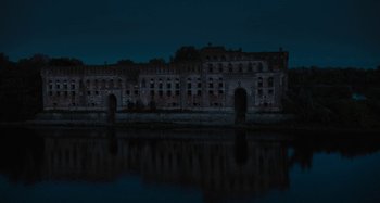 Movie still from “The Field Guide to Evil” (2018), directed by Can Evrenol – A dark picture of a building and a body of water at night time; Extreme Wide shot, High angle