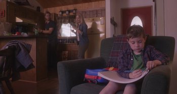 Movie still from “The Field Guide to Evil” (2018), directed by Can Evrenol – A young boy sitting on a green couch in a living room; Medium shot, Over the shoulder angle