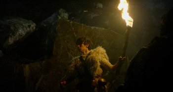 Movie still from “The Field Guide to Evil” (2018), directed by Can Evrenol – A person holding a lit up torch in the dark; Medium shot, Low angle